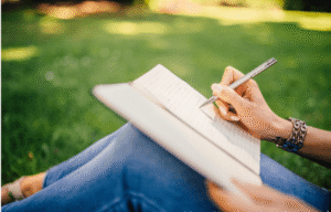 Woman sitting outside writing in a journal.