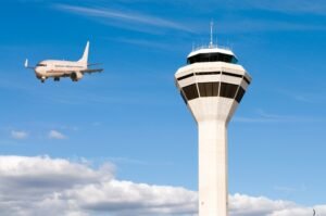 An air traffic control tower with airplane arriving (Photo: Readovia)