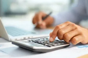 Person calculating expense using a calculator and laptop.