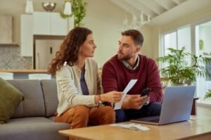 A couple reviews household bills at home, reflecting how financial stability today is often defined by managing expenses and staying afloat.