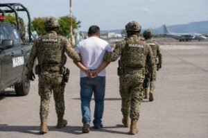 Mexican military personnel escort a detained suspect following a major operation targeting the Jalisco New Generation Cartel.
