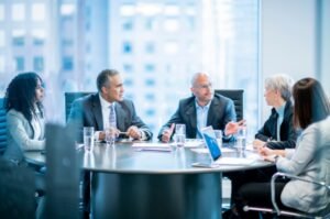 Corporate executives meet inside a modern glass-walled conference room as companies across multiple industries accelerate AI investment and restructuring efforts.