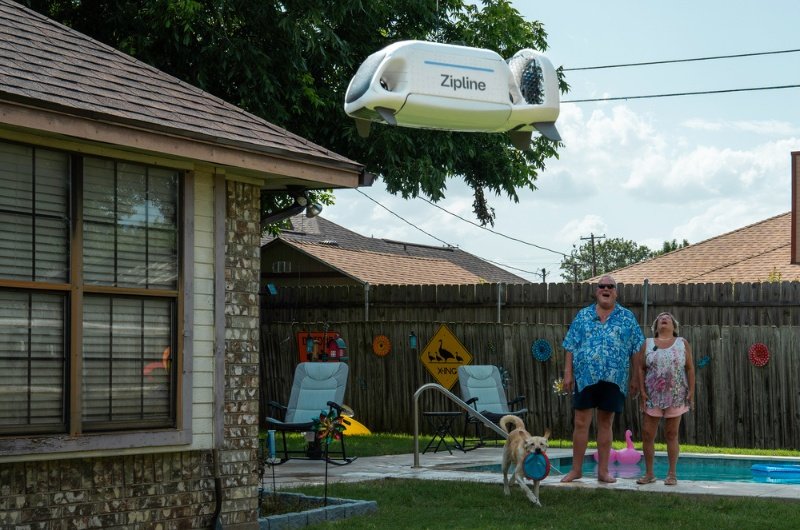 Residents watch as a Zipline delivery drone approaches with a food order during an autonomous home delivery.