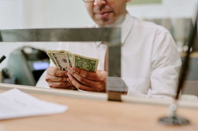 A bank teller counts cash as high-yield savings accounts offer rates far above the national average, including one account currently paying 5.00% APY.